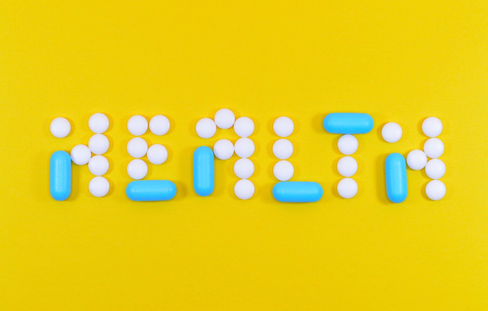 white and blue health pill and tablet letter cutout on yellow surface