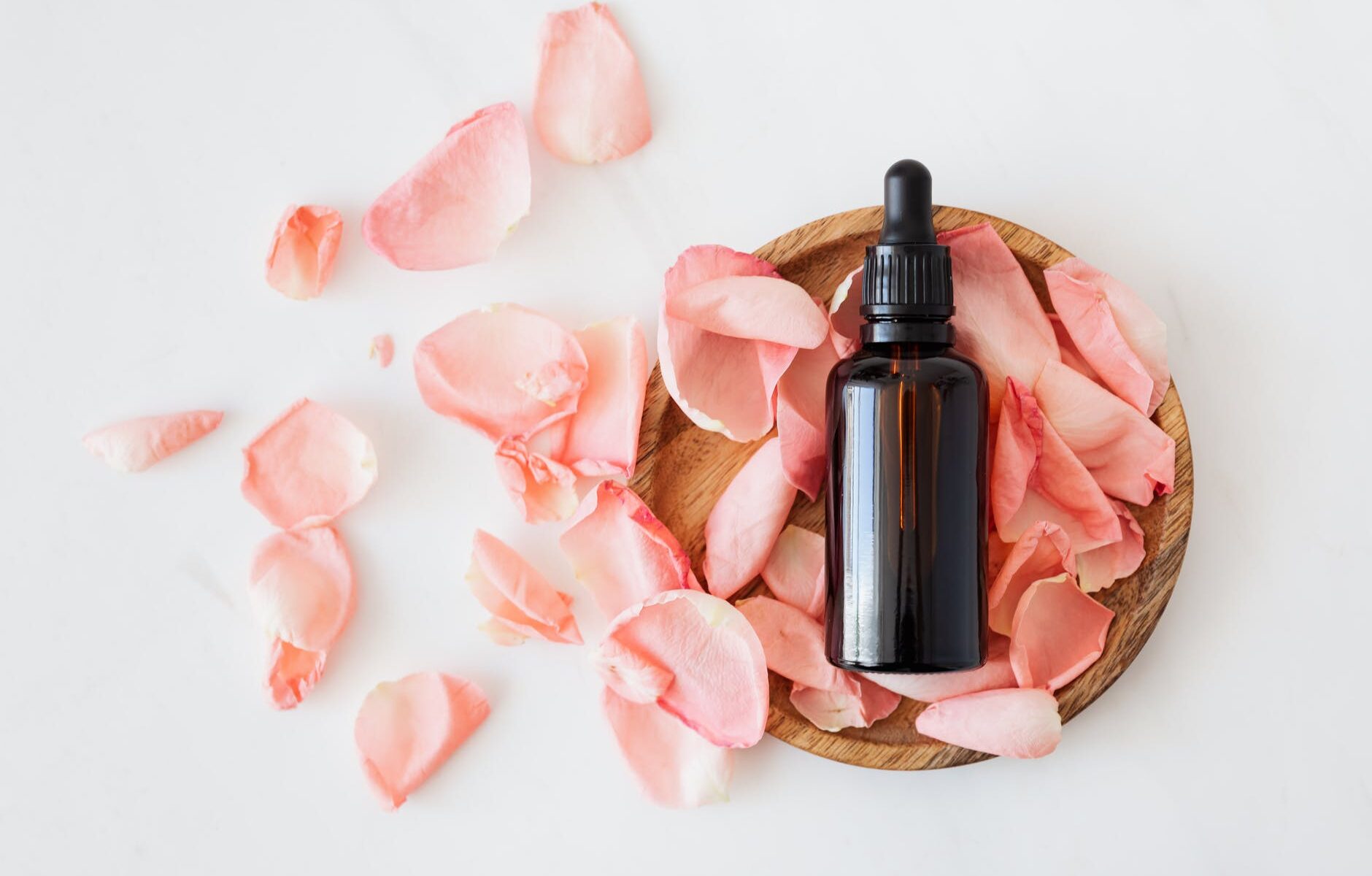 composition of cosmetic bottle with pink rose petals and wooden plate