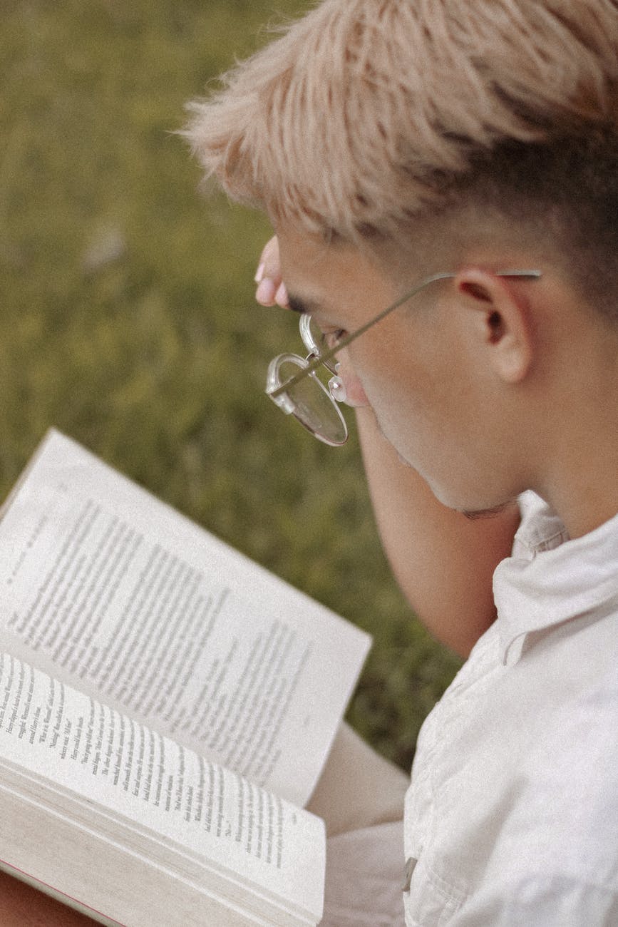 young man in glasses reading book in park