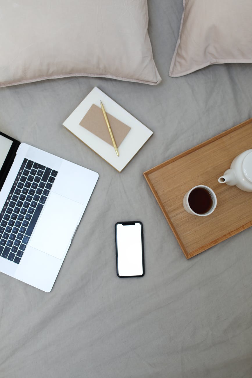 coffee cup placed on tray on bed near smartphone laptop and notebooks