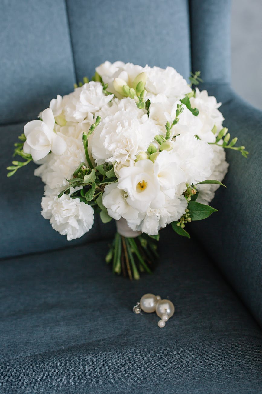 white flower bouquet on gray chair beside a pair of pearl earrings