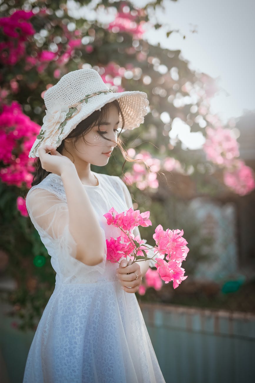 woman wearing sun hat and white dress holding pink bougainvilleas