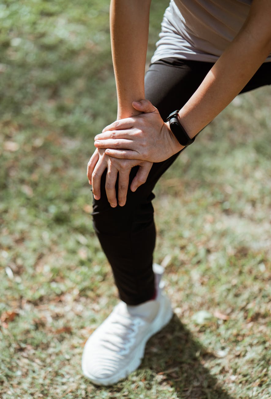 crop sportswoman stretching legs on green lawn