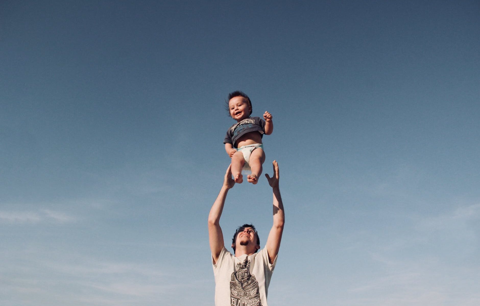 photo of man in raising baby under blue sky