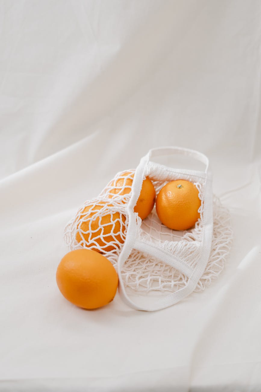 four orange fruits on white mesh bag