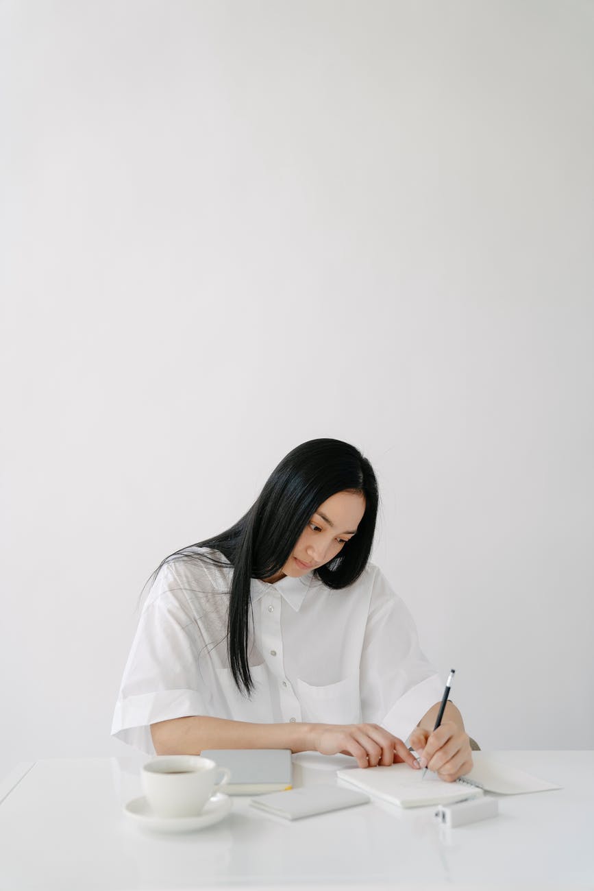 focused asian employee writing in diary at office desk