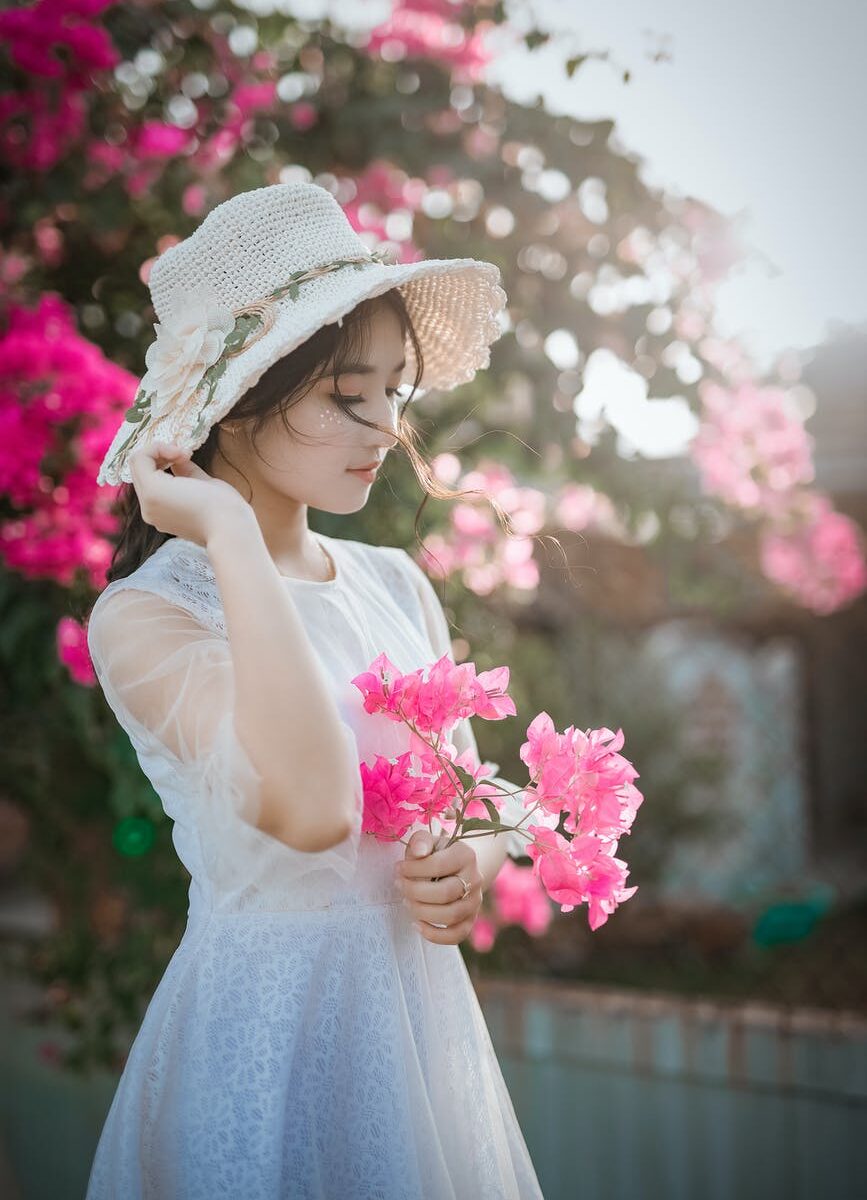 woman wearing sun hat and white dress holding pink bougainvilleas