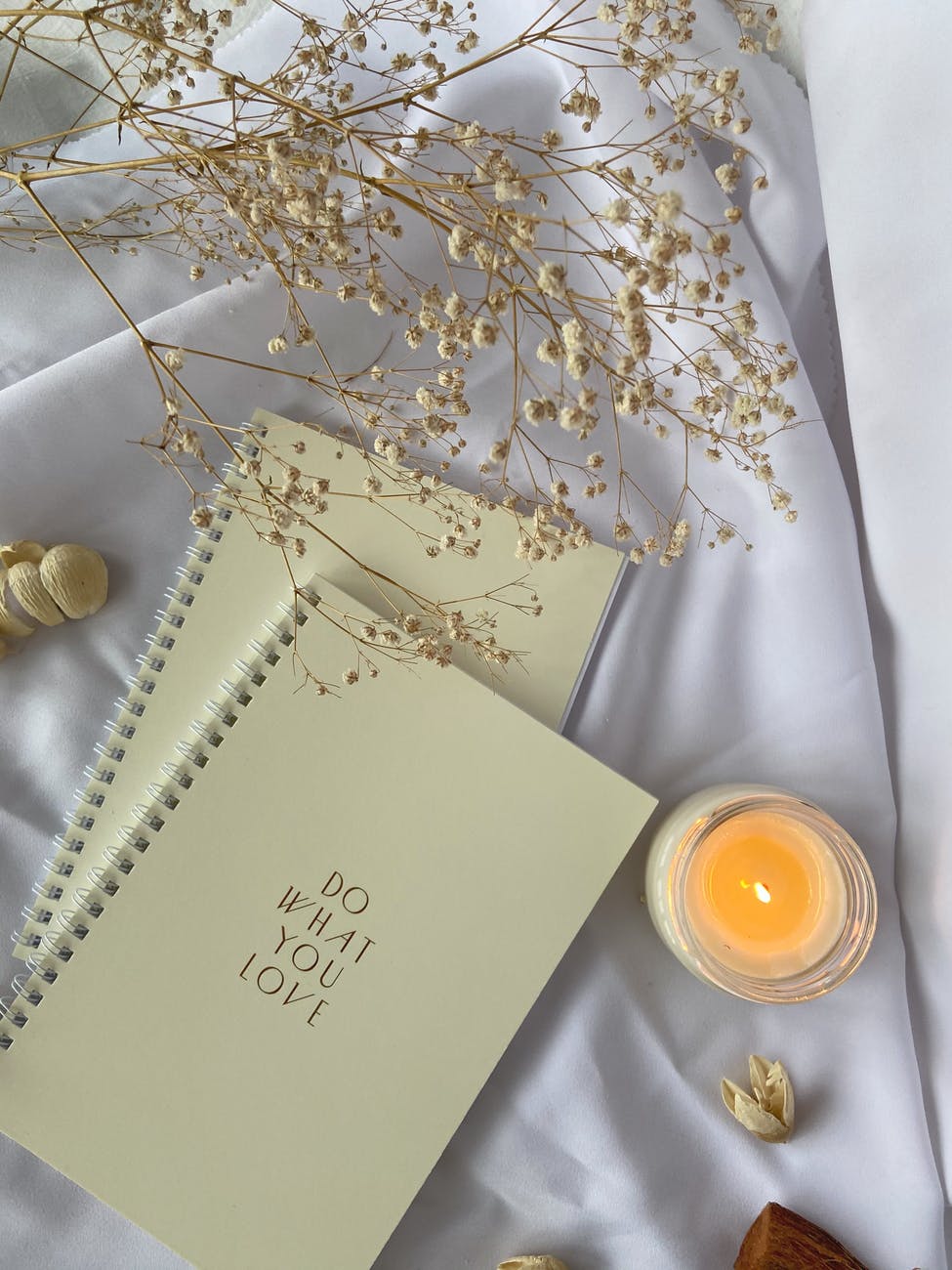 spiral notebooks placed on white cloth with burning candle